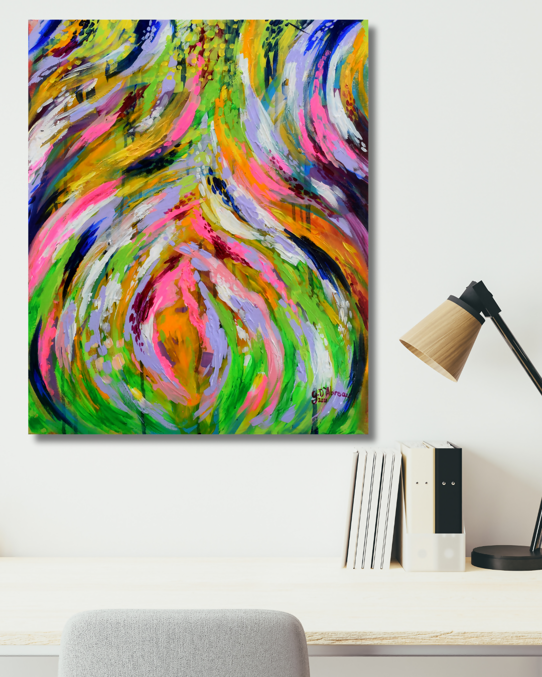 A colorful abstract canvas wall art print with swirling brushstrokes in green, pink, yellow, orange, purple, and blue, displayed on a white wall above a desk with books and a lamp.