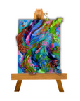 An abstract painting with swirling brushstrokes of blue, green, pink, purple, and brown, displayed on a small wooden easel against a plain white background.