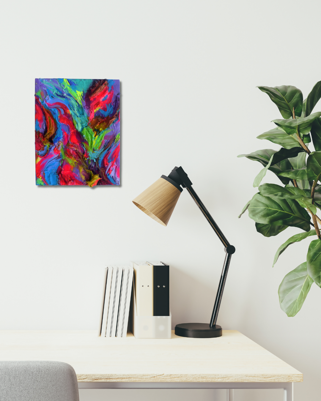 A colorful abstract canvas wall art print with swirling blue, pink, red, green, and purple paint, displayed on a white wall above a desk with a black lamp, books, and a green plant.